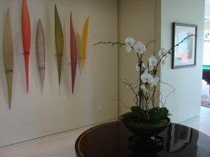 Triple stem, white, phaleonopsis orchd presented in a black ceramic bowl with willow branches, bamboo, raffia and sheets of green moss.